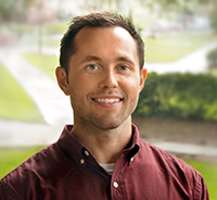 Dr. Worts smiling in a garnet shirt with grass and a sidewalk in the background