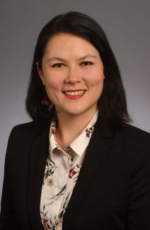 Dr. Woodbury smiling wearing a floral print button down and black blazer against a grey background