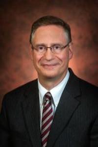Dr. Frascella smiling wearing glasses, a white button down, a garnet and gold striped tie and black jacket 