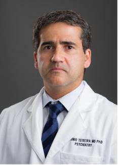 Dr. Teixeira wearing white lab coat and navy tie against dark grey background