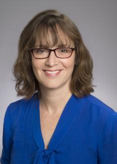 Dr. Rauch wearing a glasses and blue blouse smiling against a grey background