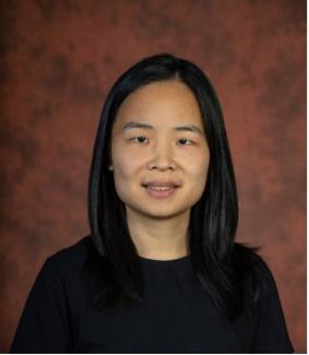 Dr Liu is sitting in front of an amber marbled background wearing a dark top.