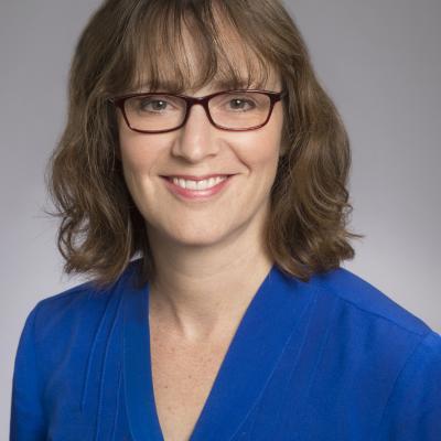 Dr. Rauch wearing a glasses and blue blouse smiling against a grey background