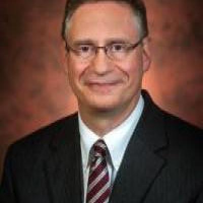 Dr. Frascella smiling wearing glasses, a white button down, a garnet and gold striped tie and black jacket 